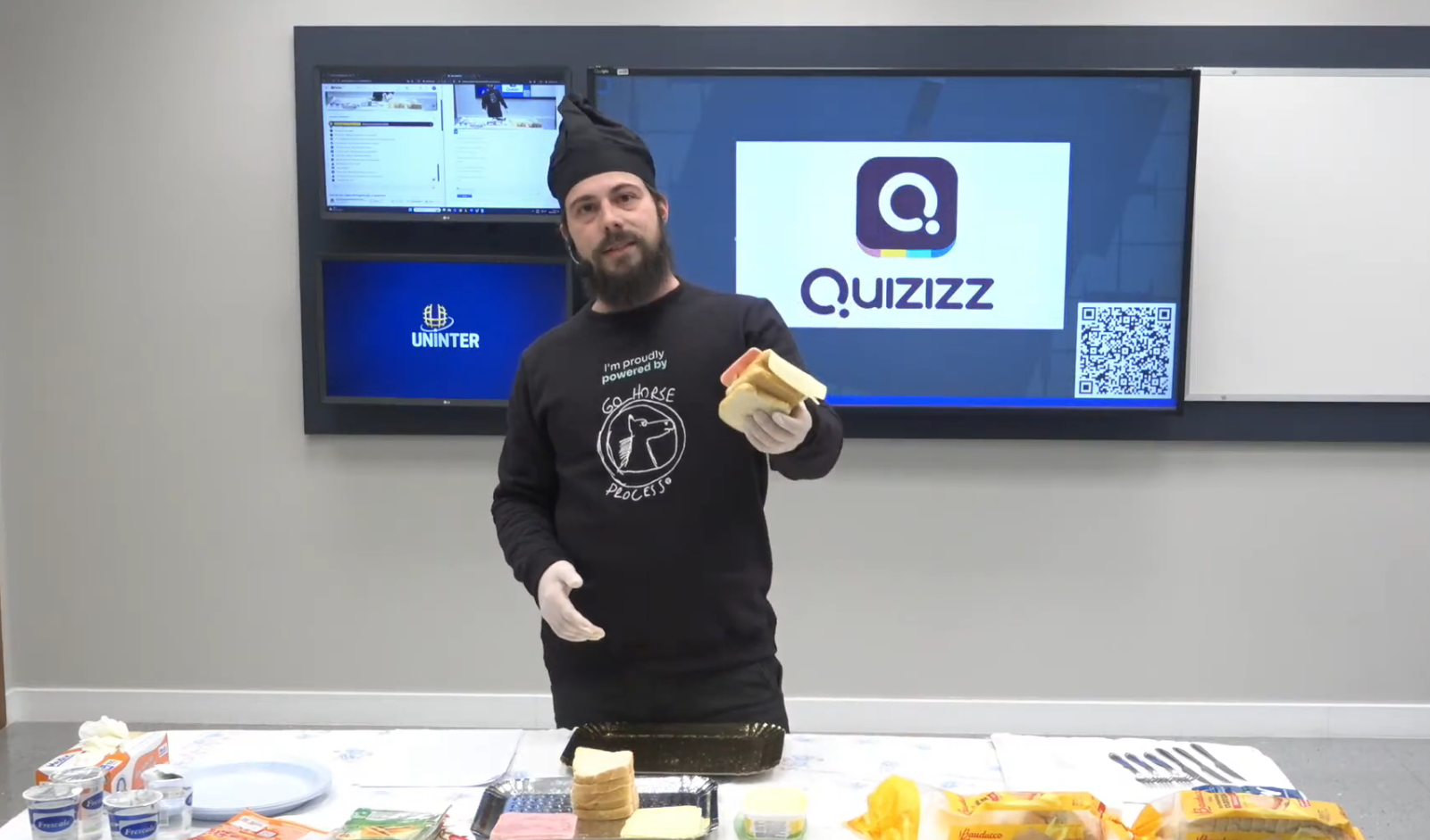 Wearing a chef hat and gloves during a live sandwich-making demo in class, with a Quizizz quiz on screen behind